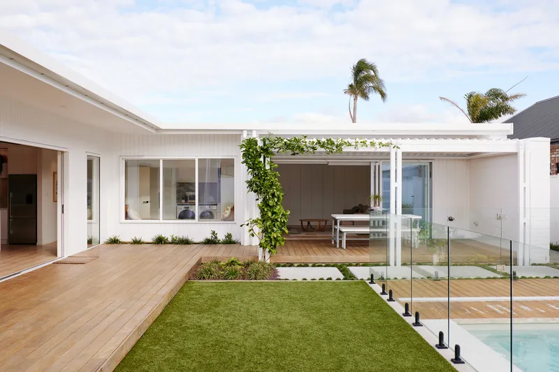 Interior courtyard with lawn, timber deck, glass-fenced pool, and pergola under palm trees