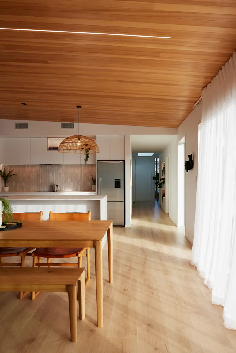 Kitchen and dining area with timber ceiling and white sheer curtains filtering natural light
