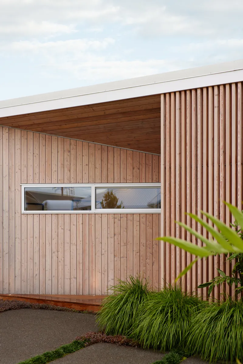 Angled timber soffit meeting vertical wood screening with white-framed horizontal windows beneath soft clouds