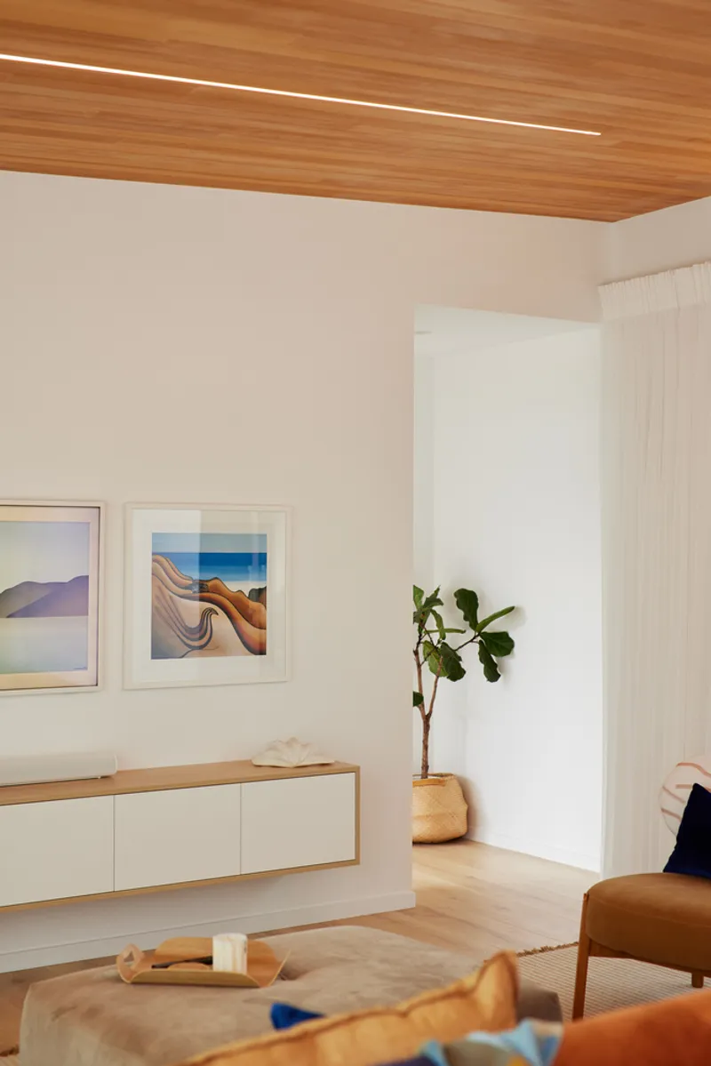 Interior corner with timber ceiling, wall-mounted credenza, potted plant and framed artworks on white walls