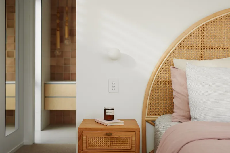 Bedroom detail showing cane headboard, bedside table and sliding door to timber-lined hallway beyond