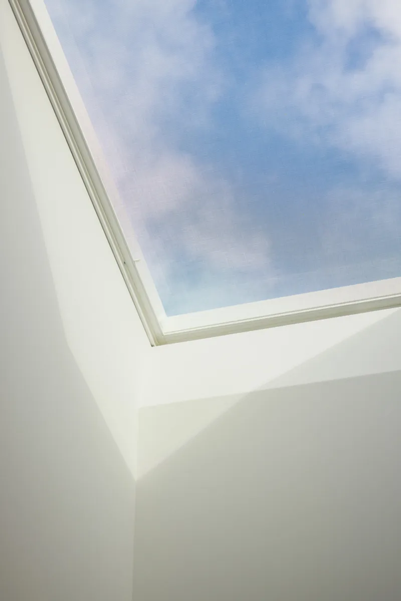 Rectangular skylight framed in white plaster walls beneath a blue sky with scattered clouds