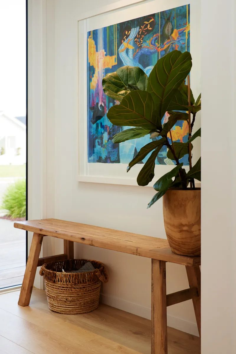Timber bench with fiddle-leaf fig in terracotta pot and woven basket below a framed artwork