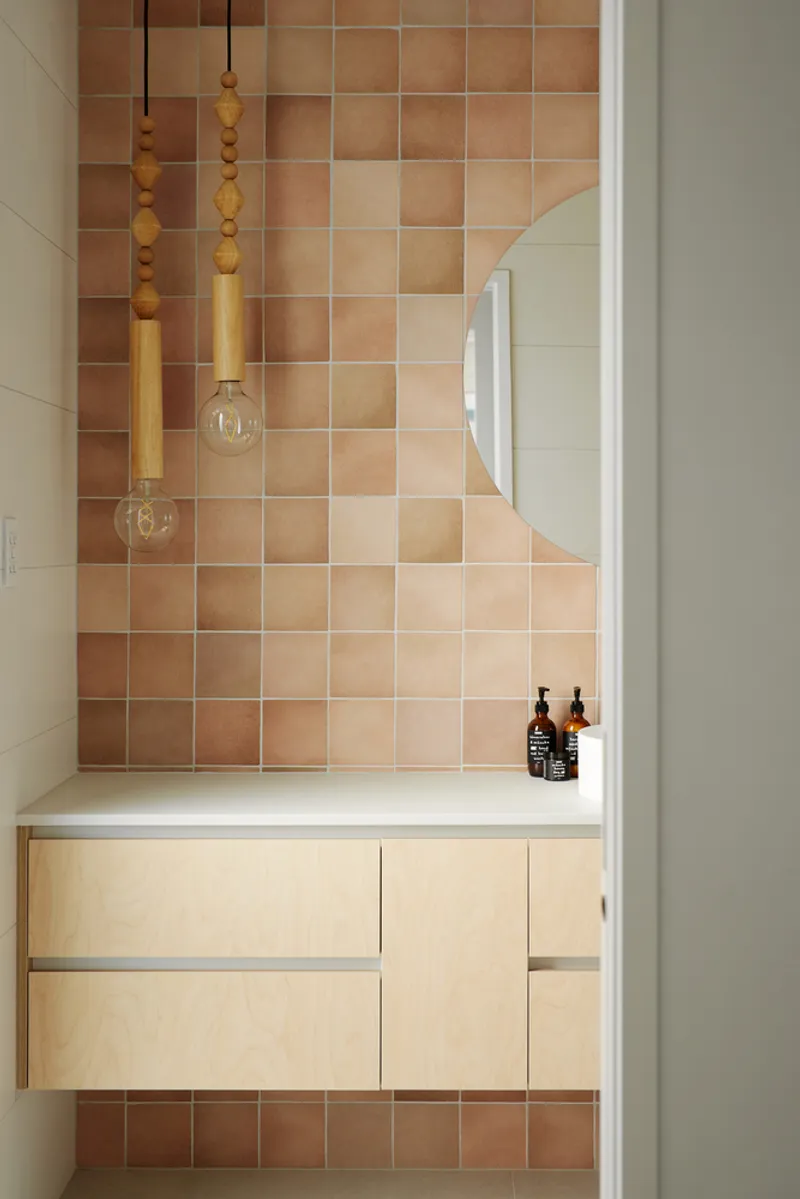 Bathroom vanity with pale plywood cabinetry beneath gradient terracotta tile wall and timber pendant lights