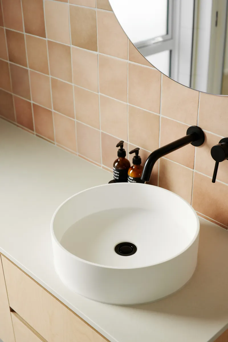 White vessel sink on plywood vanity with black wall-mounted faucet and peachy tile backsplash