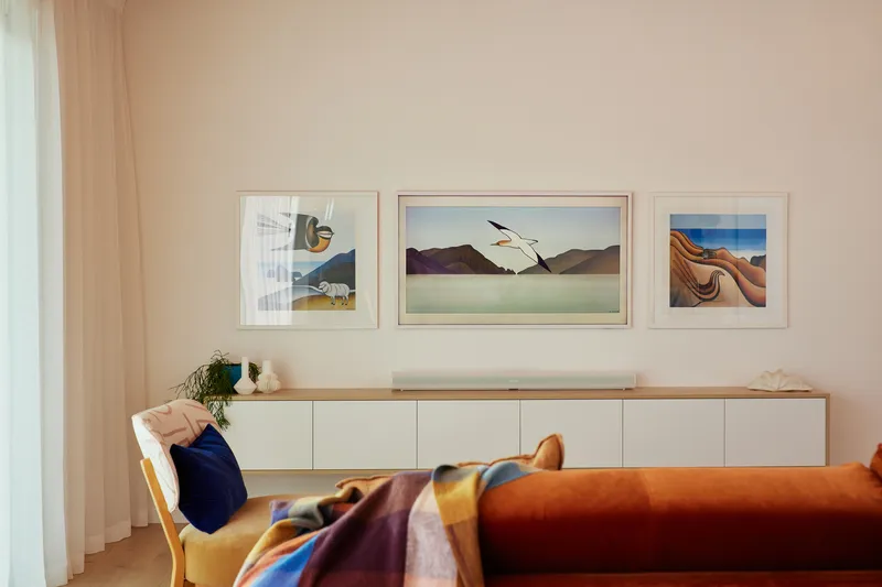 Low white storage cabinet beneath three framed prints with a figure reclining on an orange sofa