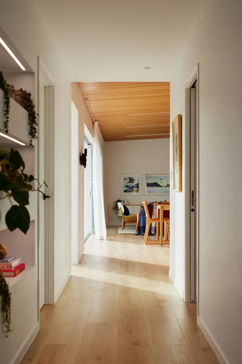 Hallway view toward dining area framed by timber ceiling panel and potted plants on shelves