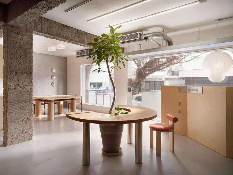 Interior with circular table around potted tree and daylight through storefront window