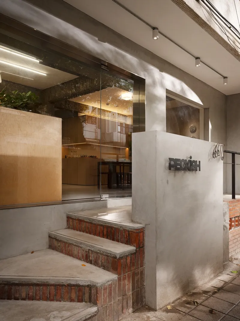 Entrance with brick and concrete steps leading to glass doors under exposed ceiling ducts
