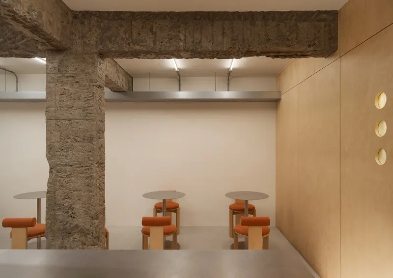 Seating alcove with exposed stone beams and circular tables flanked by orange upholstered stools