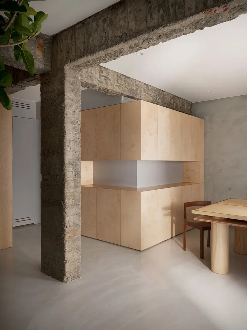 Freestanding plywood service counter beside an exposed stone column on polished concrete flooring