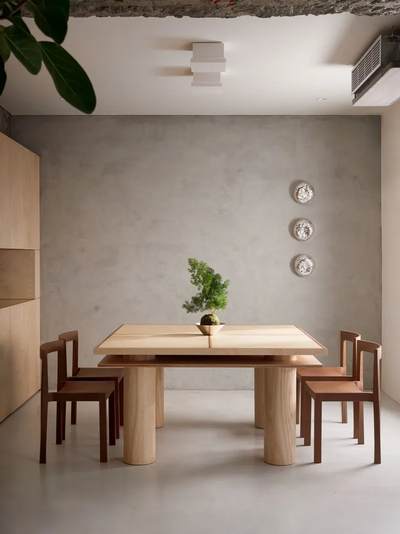 Timber dining table with cylindrical legs centered against a grey plastered wall with three circular wall sconces