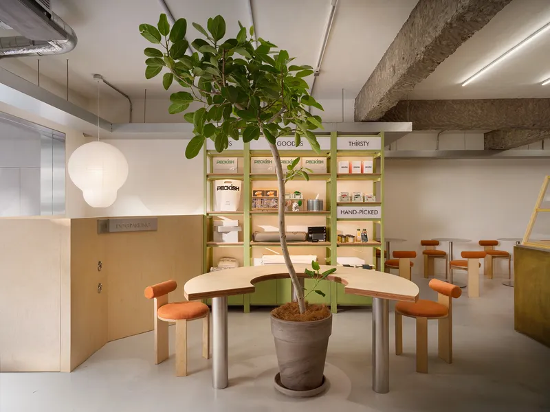 Curved communal table wrapping around a potted tree near a green shelving unit with product displays