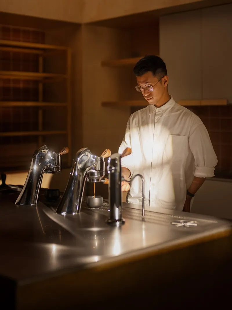 Barista working at stainless steel espresso counter under warm ambient lighting