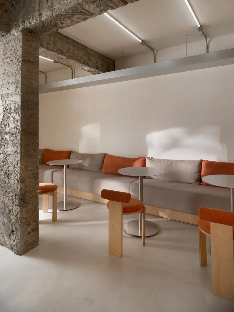 Banquette seating with orange cushions and round pedestal tables beside rough concrete column
