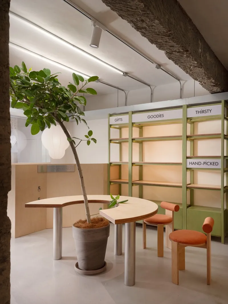 Interior seating area with green shelving units, potted tree and exposed concrete beam overhead