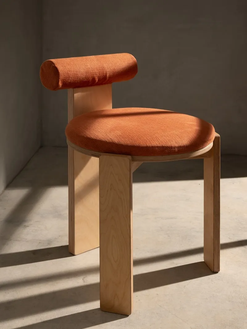 Orange upholstered chair with curved backrest and timber frame in direct sunlight