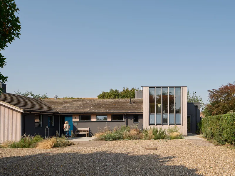 Front entry approach across gravel drive showing vertical glazed pavilion and planted garden beds