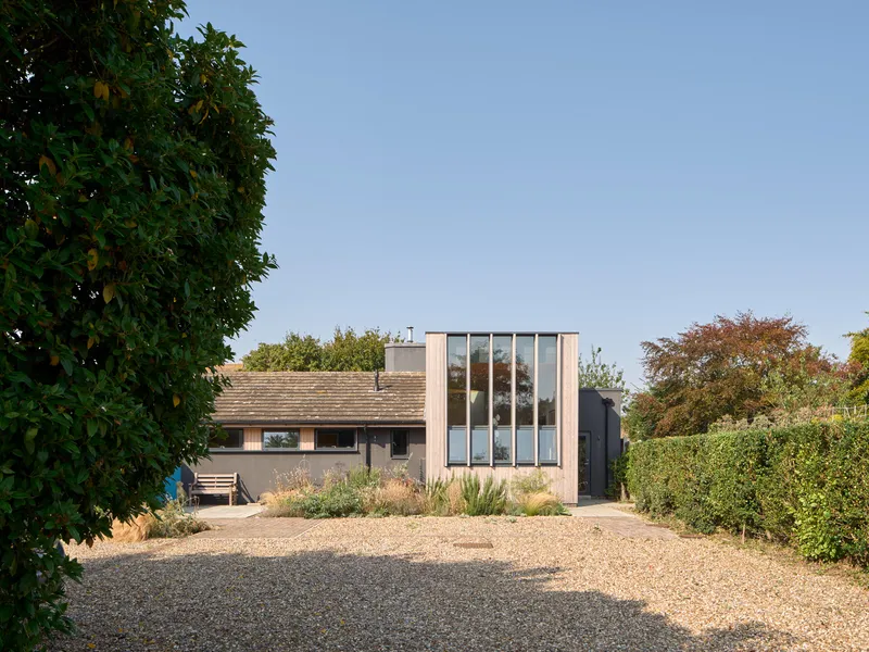 Entry elevation with vertical window mullions and gravel forecourt framed by hedges and trees