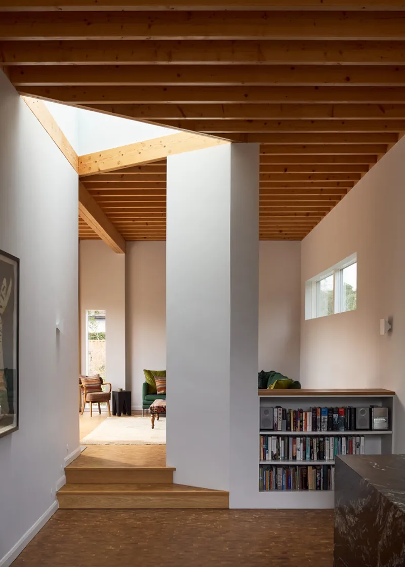 Interior hallway with timber steps, skylight above and built-in bookshelf beside painted column