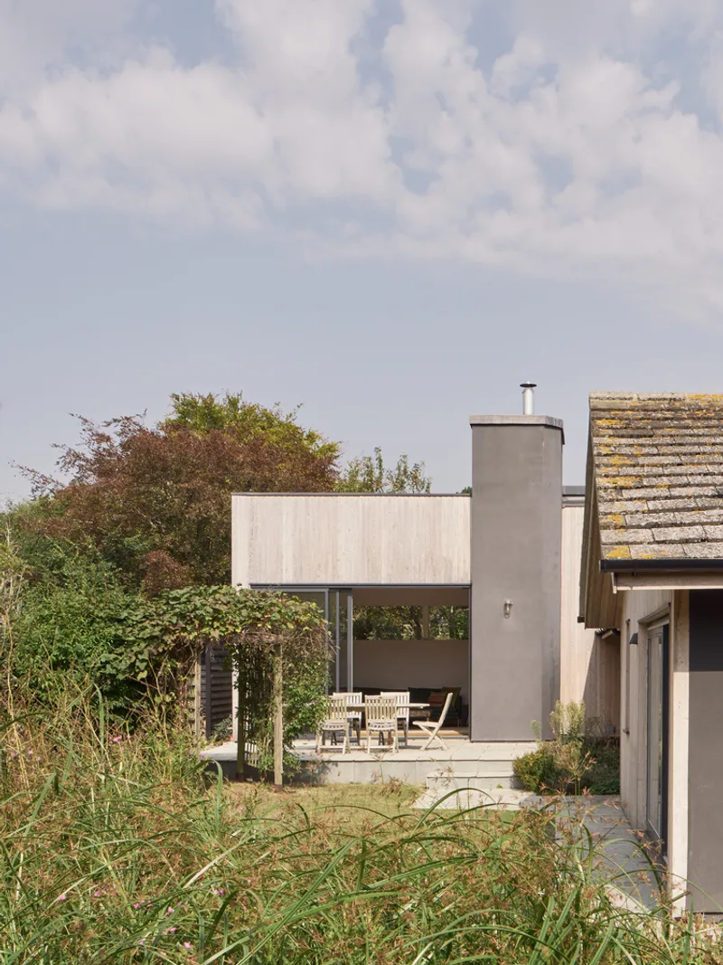Exterior view of concrete volumes framing a terrace surrounded by tall grasses and mature trees