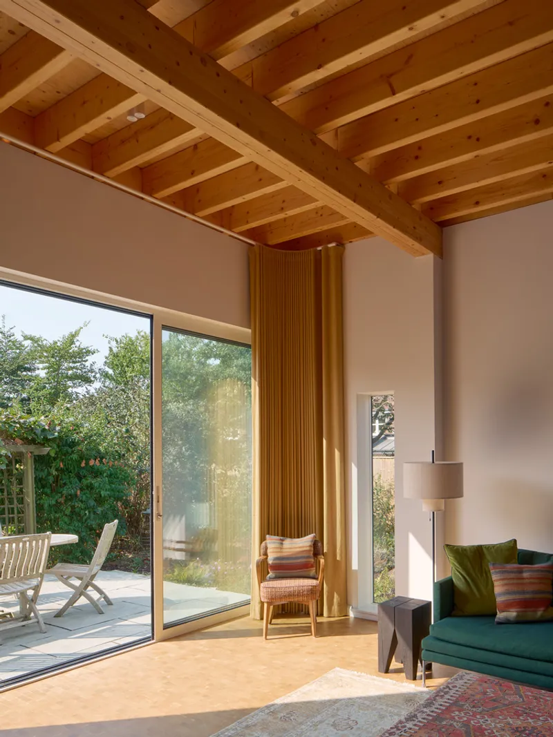 Living room with exposed timber joist ceiling and full-height glazing overlooking the terrace in afternoon sun