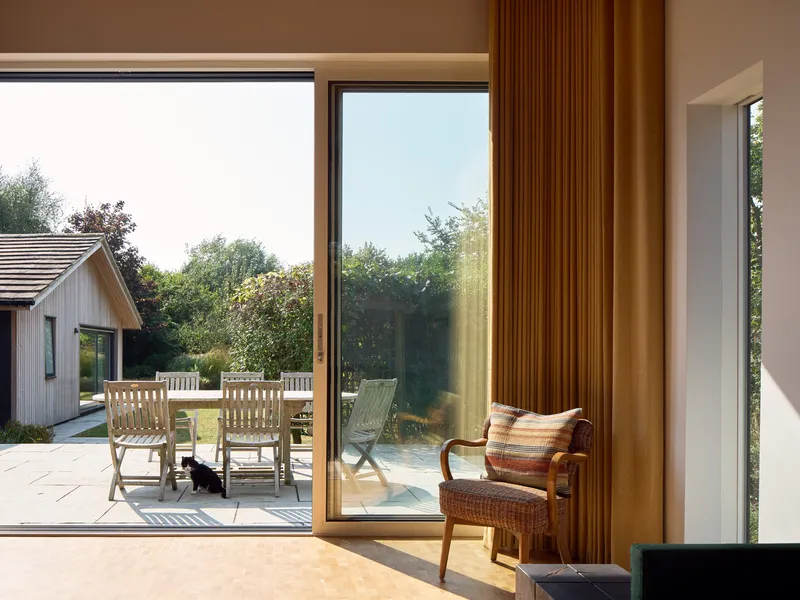 Corner glazing with vertical timber curtain framing views to the terrace and outdoor dining area
