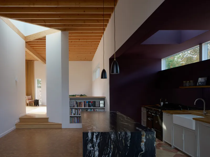 Kitchen with dark marbled stone island beneath exposed timber ceiling and pendant lights