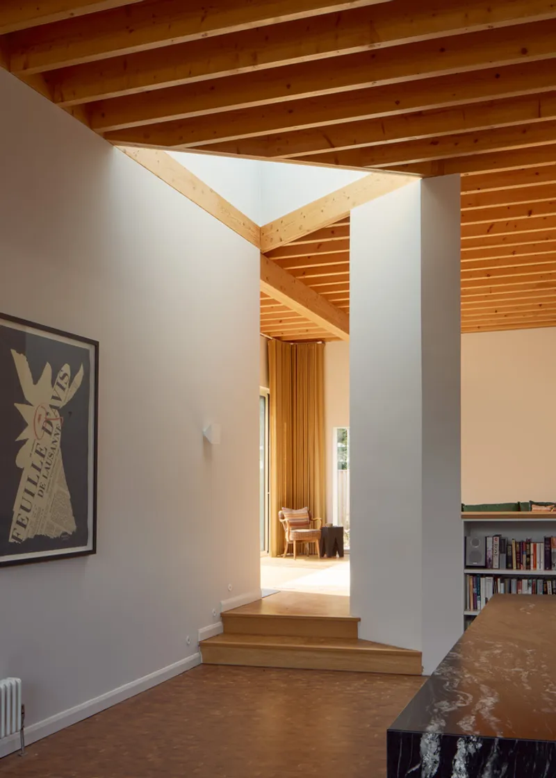 Interior hallway with timber steps rising toward rooms beneath exposed wood beam ceiling and skylight