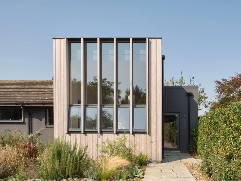 Garden facade showing vertical timber cladding with tall glazed window bays and planted borders