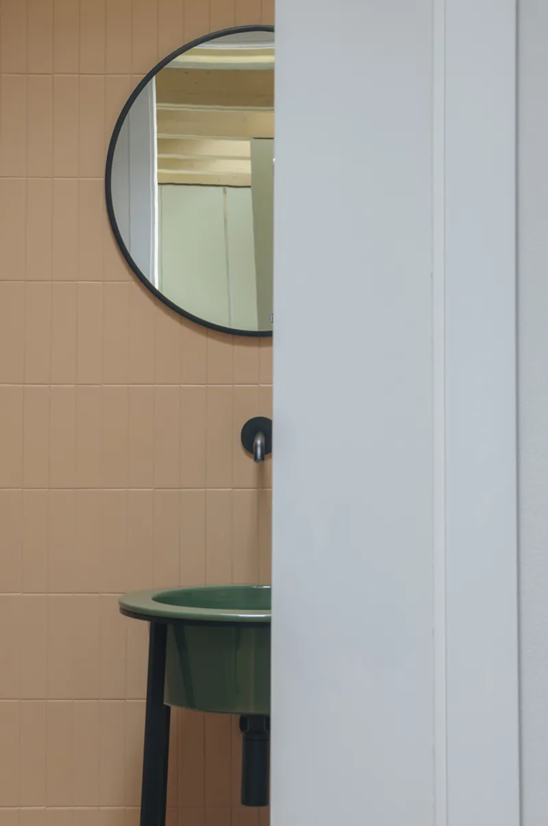 Half-round mirror above a green basin on beige tile wall with white door frame