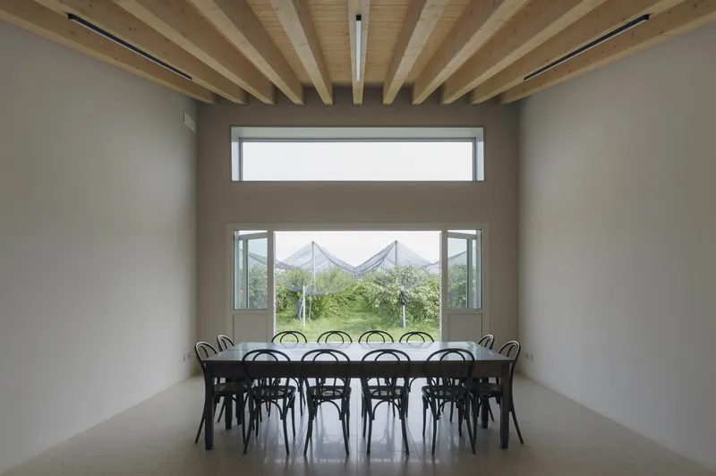 Dining room with exposed timber ceiling beams and windows overlooking orchard rows