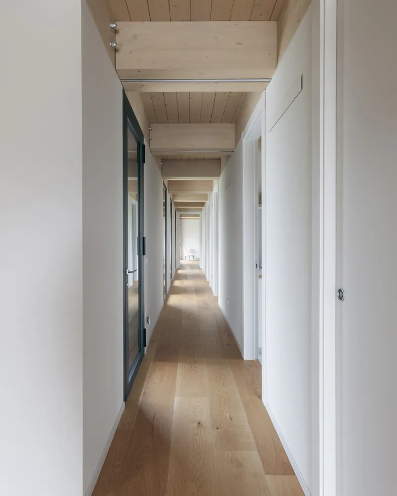 Long interior corridor with exposed timber ceiling beams and white walls flanking both sides