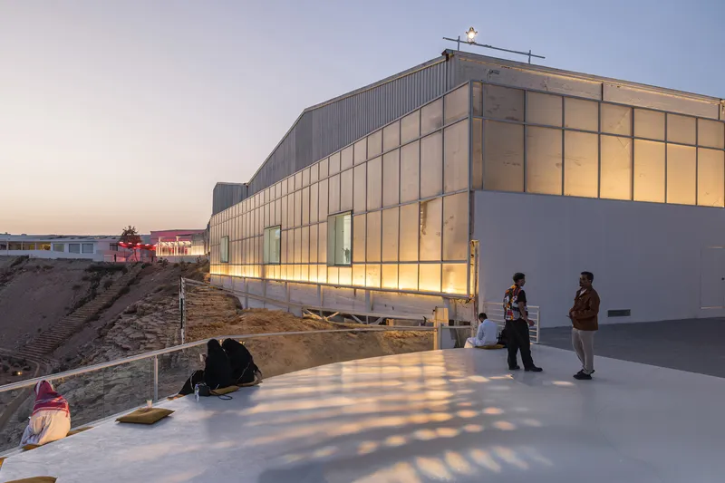 Elevated terrace with visitors gathering at dusk beside the illuminated translucent facade