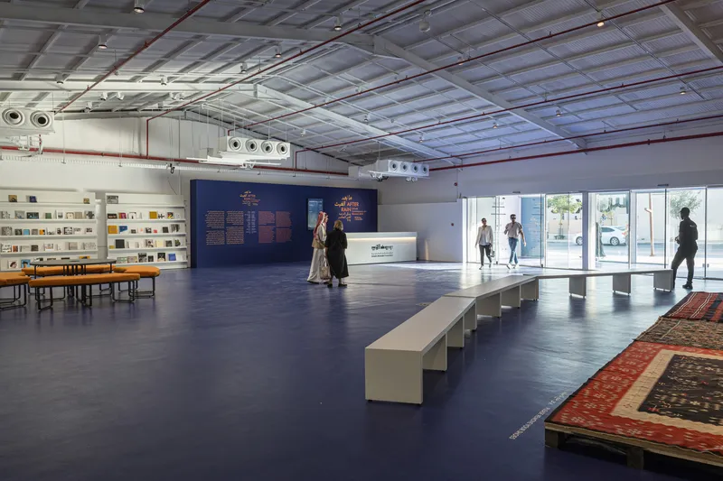 Gallery space with exposed corrugated metal ceiling and visitors walking past wall-mounted displays