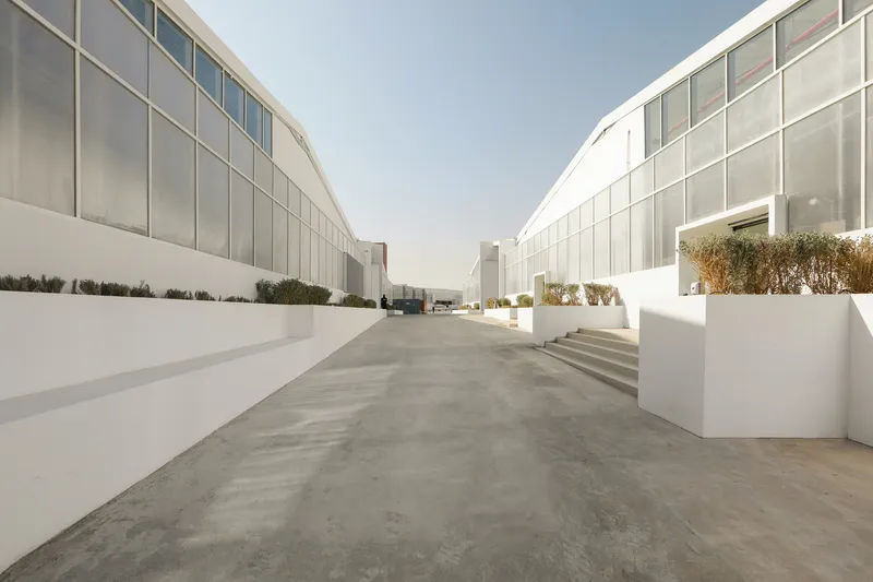 Concrete courtyard flanked by two curved glass and panel pavilion volumes under white planters