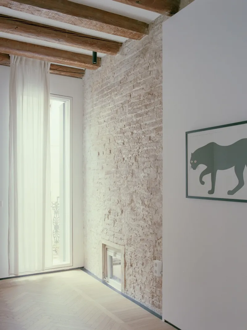 Room corner with exposed brick wall, timber ceiling beams, and a tall window with white curtains