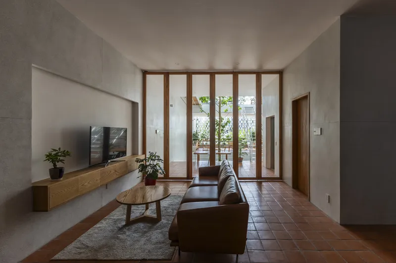 Living room with terracotta tile floor, timber-framed glass doors opening to a terrace, and concrete walls