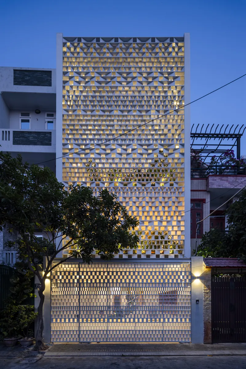 Street view of the perforated brick facade illuminated from within at dusk