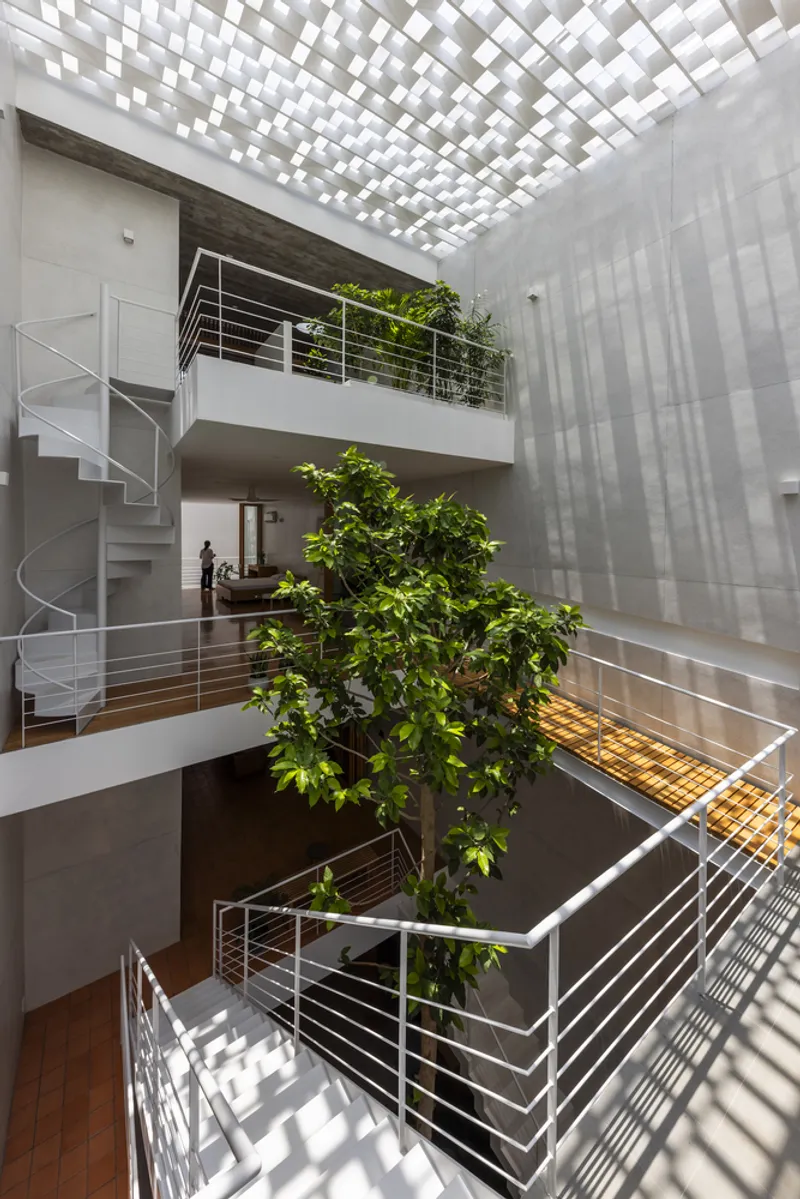 Triple-height atrium with spiral stair, tree growing through levels, and chequered skylight casting shadows