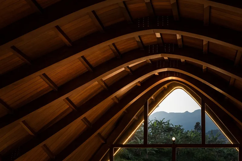 Interior view of laminated timber arches and wood ceiling framing a mountain view through peaked window