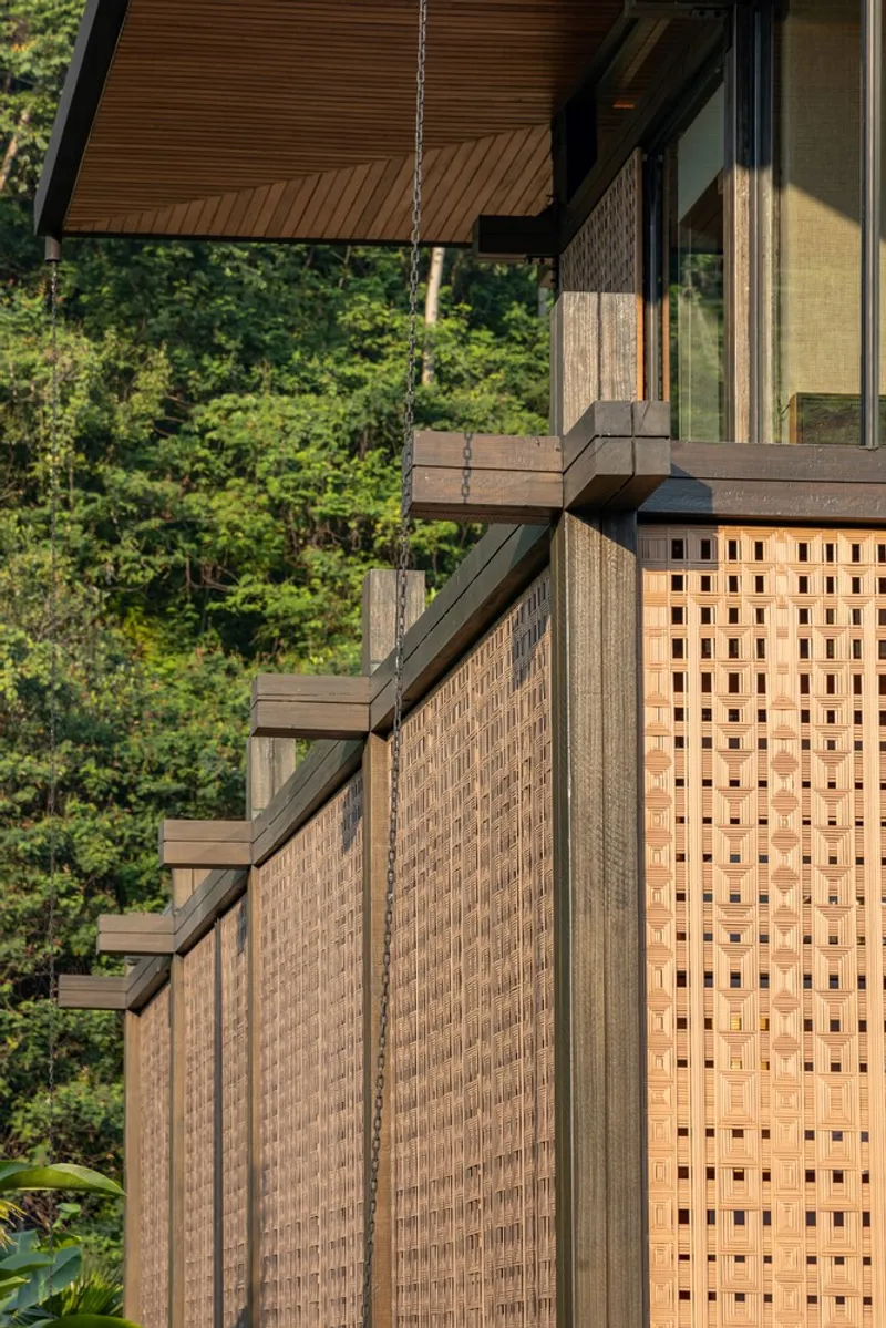 Woven timber screen panels with horizontal beam details beneath a covered porch against dense forest
