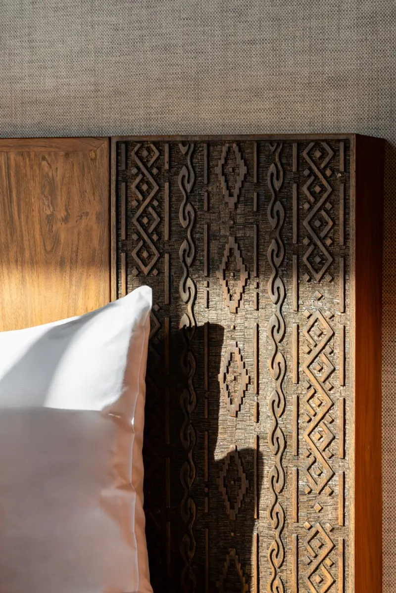 Timber headboard with carved geometric pattern beside a white pillow
