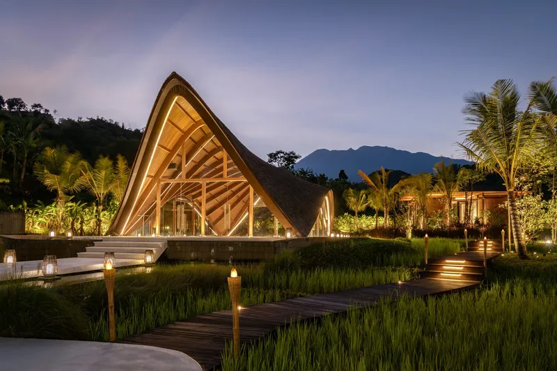 Peaked pavilion with exposed timber trusses across a reflecting pool at twilight
