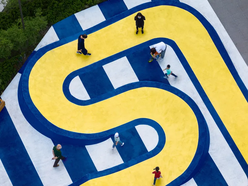 Overhead view of painted yellow and blue basketball court with children playing under afternoon sun