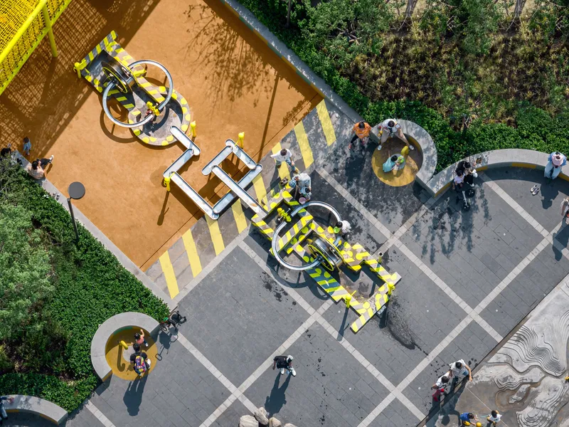 Aerial view of playground equipment and yellow striped pavement with children in dappled tree shade
