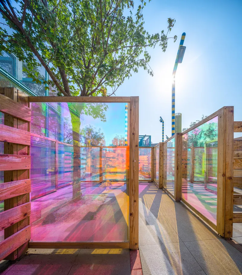 Dichroic glass panels in timber frames casting rainbow reflections on the pathway below