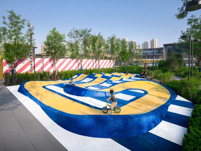 Yellow and blue patterned play surface with child cycling and striped perimeter fence
