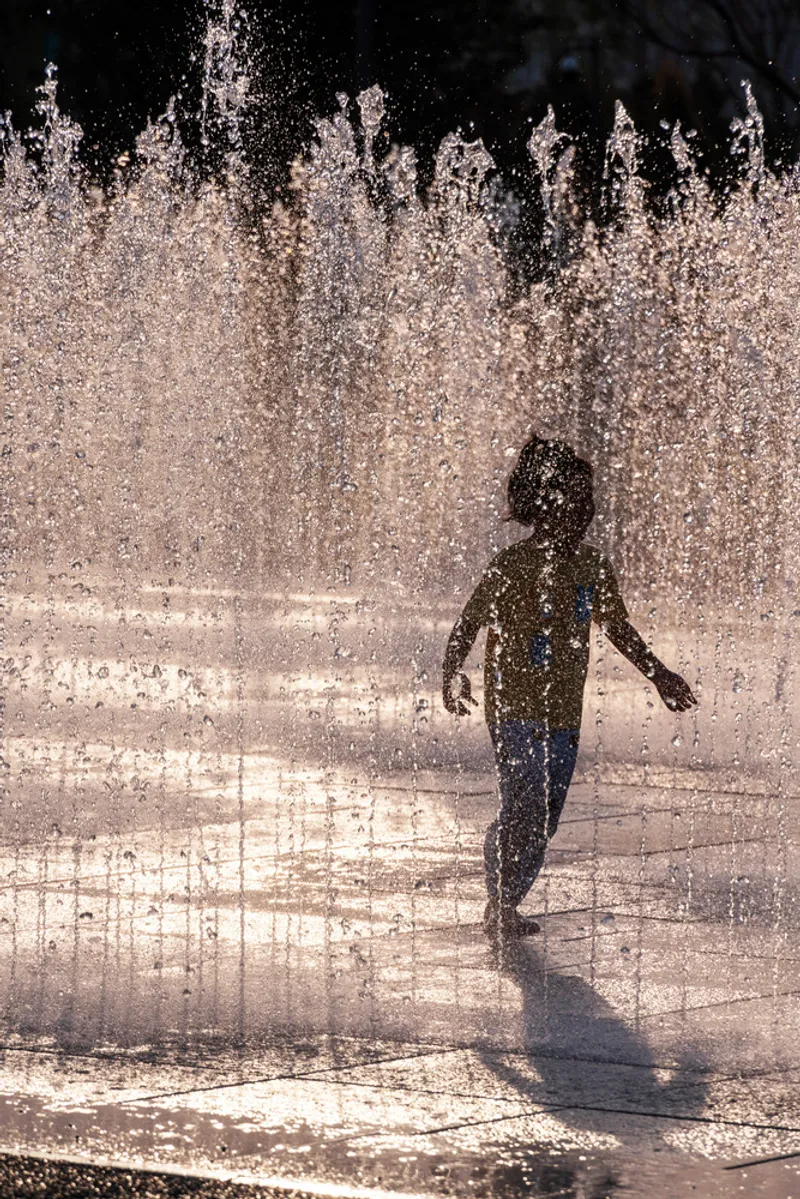 Child walking through the spray fountain jets in bright midday sun