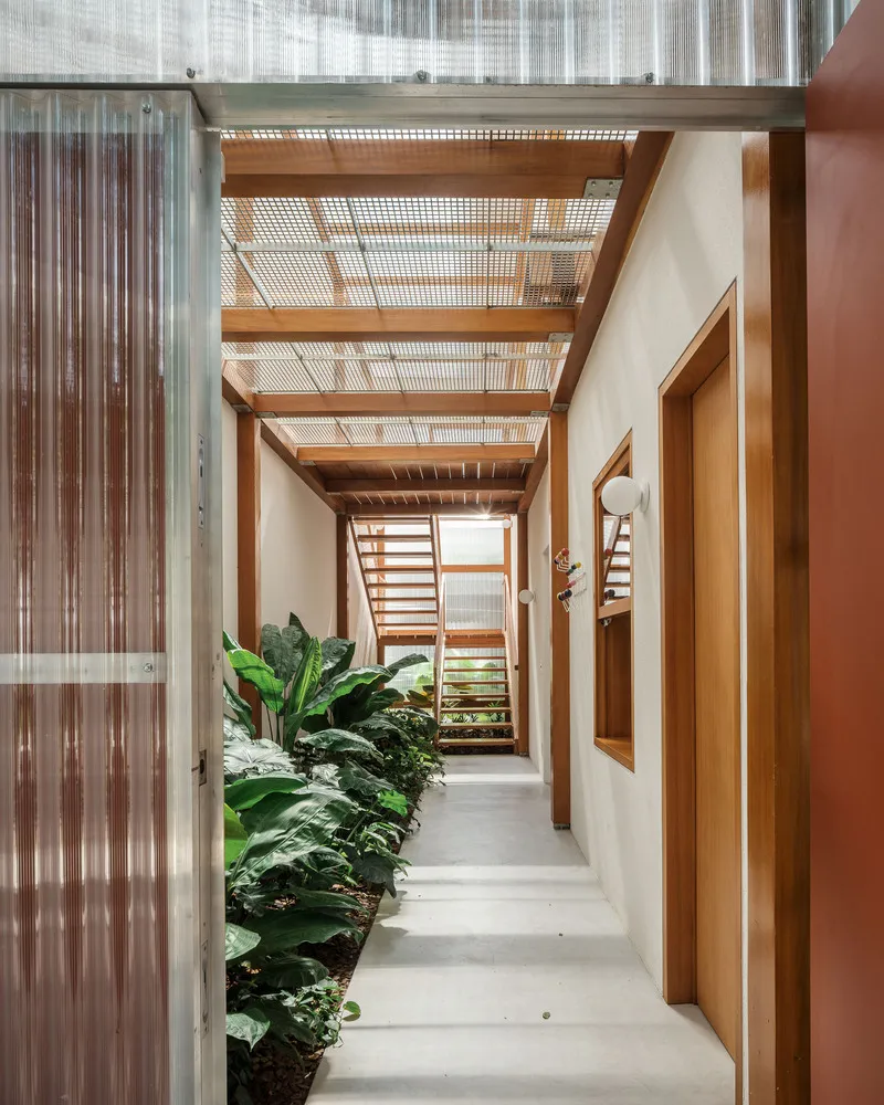 Interior corridor with timber pergola overhead, planted beds along corrugated metal wall and polished concrete floor